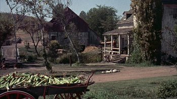 Movie still from “Friendly Persuasion” (1956), directed by William Wyler – A wagon filled with corn sitting on top of a dirt road; Extreme Wide shot, High angle