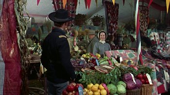 Movie still from “Friendly Persuasion” (1956), directed by William Wyler – A man standing next to a woman in front of a table full of fruit; Medium shot, Over the shoulder angle
