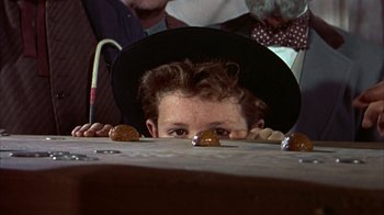 Movie still from “Friendly Persuasion” (1956), directed by William Wyler – A man in a black hat is hiding behind a table; Close Up shot, Over the shoulder angle