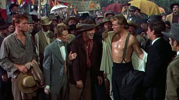 Movie still from “Friendly Persuasion” (1956), directed by William Wyler – A group of men standing next to each other on a street; Medium shot, Over the shoulder angle