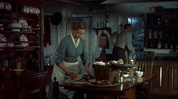 Movie still from “Friendly Persuasion” (1956), directed by William Wyler – A woman is cutting bread in a kitchen; Medium shot, Low angle