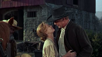 Movie still from “Friendly Persuasion” (1956), directed by William Wyler – A man and a woman standing next to each other in front of a stone building; Medium shot, Low angle