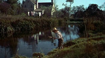 Movie still from “Friendly Persuasion” (1956), directed by William Wyler – A man standing on the side of a river holding a fishing pole; Wide shot, Low angle