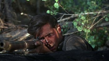 Movie still from “Friendly Persuasion” (1956), directed by William Wyler – A man is aiming a rifle in the woods; Close Up shot, High angle