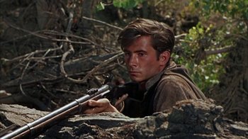 Movie still from “Friendly Persuasion” (1956), directed by William Wyler – A young man is holding a rifle in the woods; Close Up shot, High angle