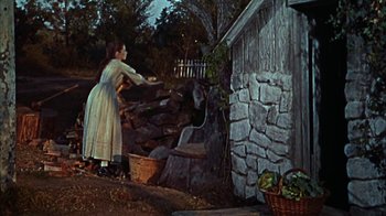 Movie still from “Friendly Persuasion” (1956), directed by William Wyler – A woman in a white dress standing next to a pile of wood; Wide shot, Low angle