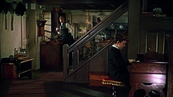 Movie still from “Friendly Persuasion” (1956), directed by William Wyler – A man sitting on a chair next to a staircase; Wide shot, High angle
