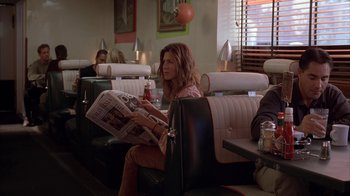 Movie still from “Friends with Money” (2006), directed by Nicole Holofcener – A woman sitting in a booth reading a newspaper; Medium shot, Over the shoulder angle