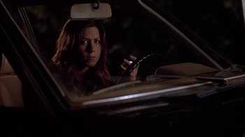 Movie still from “Friends with Money” (2006), directed by Nicole Holofcener – A woman sitting in the driver's seat of a car while holding a cell phone; Medium shot, Over the shoulder angle