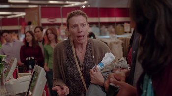 Movie still from “Friends with Money” (2006), directed by Nicole Holofcener – A woman holding a bag of newspapers in a store; Medium shot, Over the shoulder angle