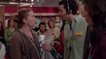 Movie still from “Friends with Money” (2006), directed by Nicole Holofcener – A man and a woman talking to each other in front of a group of people; Medium shot, Over the shoulder angle