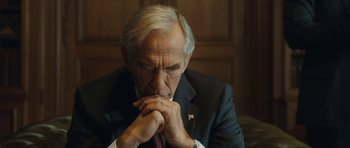 Movie still from “From Paris with Love” (2010), directed by Pierre Morel – An older man wearing a suit and tie with his hands clasped together; Close Up shot, High angle
