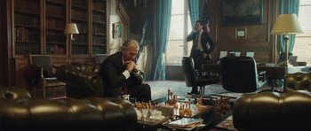 Movie still from “From Paris with Love” (2010), directed by Pierre Morel – A man sitting in front of a chess board in a room; Wide shot, Over the shoulder angle
