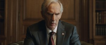 Movie still from “From Paris with Love” (2010), directed by Pierre Morel – An older man wearing a suit and tie; Close Up shot, Over the shoulder angle