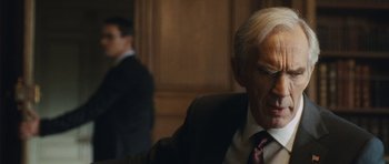 Movie still from “From Paris with Love” (2010), directed by Pierre Morel – An older man wearing a suit and tie; Close Up shot, Over the shoulder angle