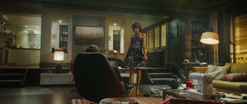 Movie still from “From Paris with Love” (2010), directed by Pierre Morel – A woman in a black dress standing in front of a man in a chair; Wide shot, Over the shoulder angle