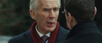 Movie still from “From Paris with Love” (2010), directed by Pierre Morel – An older man wearing a suit and tie talking to another man; Close Up shot, Over the shoulder angle