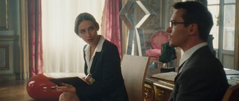 Movie still from “From Paris with Love” (2010), directed by Pierre Morel – A woman sitting in front of a chair in a room; Medium shot, Over the shoulder angle