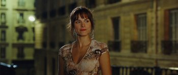 Movie still from “From Paris with Love” (2010), directed by Pierre Morel – A woman standing in front of a building at night; Close Up shot, Over the shoulder angle