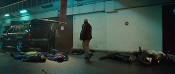 Movie still from “From Paris with Love” (2010), directed by Pierre Morel – A group of dead bodies laying on the ground next to a building; Wide shot, High angle