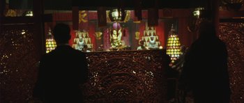 Movie still from “From Paris with Love” (2010), directed by Pierre Morel – A wooden carving in front of an image of a temple; Wide shot, Over the shoulder angle