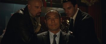 Movie still from “From Paris with Love” (2010), directed by Pierre Morel – A man in a suit and tie with two other men; Close Up shot, Over the shoulder angle