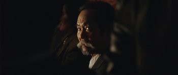 Movie still from “From Paris with Love” (2010), directed by Pierre Morel – A man with a beard and mustache is looking at the camera; Close Up shot, Over the shoulder angle