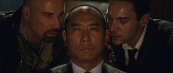 Movie still from “From Paris with Love” (2010), directed by Pierre Morel – A man in a suit and tie with two other men; Close Up shot, Over the shoulder angle