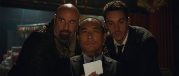 Movie still from “From Paris with Love” (2010), directed by Pierre Morel – A group of men standing next to each other holding a piece of paper; Close Up shot, Low angle