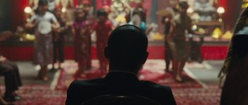 Movie still from “From Paris with Love” (2010), directed by Pierre Morel – A man sitting in front of a group of people; Medium shot, Over the shoulder angle
