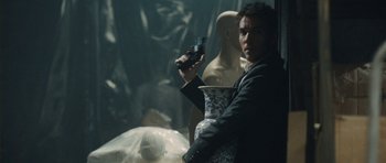 Movie still from “From Paris with Love” (2010), directed by Pierre Morel – A man holding a gun while standing in front of mannequins; Medium shot, Over the shoulder angle
