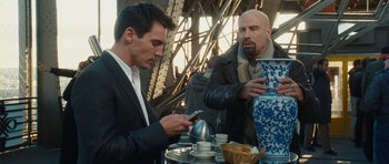 Movie still from “From Paris with Love” (2010), directed by Pierre Morel – Two men are looking at their cell phones at an outdoor cafe; Medium shot, Low angle