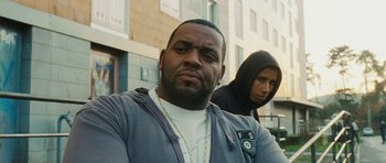 Movie still from “From Paris with Love” (2010), directed by Pierre Morel – A man and a woman standing next to each other in front of a building; Close Up shot, Low angle