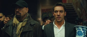 Movie still from “From Paris with Love” (2010), directed by Pierre Morel – A man holding a gun while standing next to another man; Close Up shot, Low angle