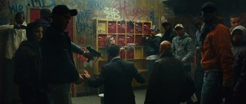 Movie still from “From Paris with Love” (2010), directed by Pierre Morel – A group of people standing in front of a wall with graffiti on it; Wide shot, High angle