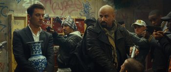 Movie still from “From Paris with Love” (2010), directed by Pierre Morel – A man with a bald head is pointing to something; Medium shot, Over the shoulder angle