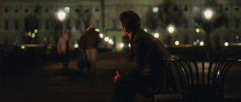 Movie still from “From Paris with Love” (2010), directed by Pierre Morel – A man sitting on top of a bench at night; Wide shot, Over the shoulder angle
