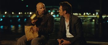 Movie still from “From Paris with Love” (2010), directed by Pierre Morel – Two men sitting on the ground talking to each other; Medium shot, Over the shoulder angle