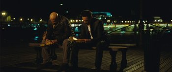 Movie still from “From Paris with Love” (2010), directed by Pierre Morel – Two men are sitting on a bench reading a book at night; Medium shot, High angle