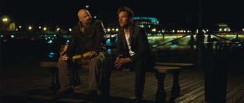 Movie still from “From Paris with Love” (2010), directed by Pierre Morel – Two men sitting on a bench at night; Medium shot, Over the shoulder angle