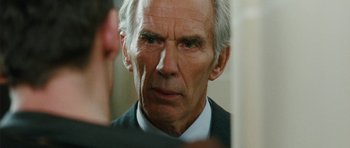 Movie still from “From Paris with Love” (2010), directed by Pierre Morel – An older man in a white shirt and black jacket; Close Up shot, Over the shoulder angle