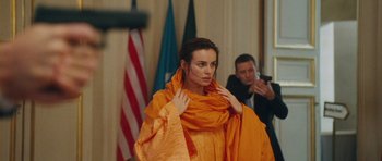 Movie still from “From Paris with Love” (2010), directed by Pierre Morel – A woman in an orange dress holding a scarf; Medium shot, Over the shoulder angle