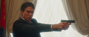Movie still from “From Paris with Love” (2010), directed by Pierre Morel – A man in a suit and tie holding a gun in his hand; Medium shot, Low angle