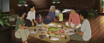 Movie still from “Funan” (2018), directed by Denis Do – A group of people sitting around a table with food on top of it; Wide shot, High angle