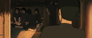 Movie still from “Funan” (2018), directed by Denis Do – A group of people sitting in a dark room; Medium shot, High angle