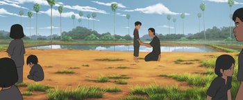 Movie still from “Funan” (2018), directed by Denis Do – A man kneeling down next to a young boy; Wide shot, High angle