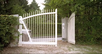 Movie still from “Funny Games” (1997), directed by Michael Haneke – An open white gate in the middle of a driveway; Extreme Wide shot, Low angle