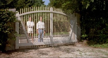 Movie still from “Funny Games” (1997), directed by Michael Haneke – Two people standing in front of an open white gate; Wide shot, Low angle