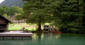 Movie still from “Funny Games” (1997), directed by Michael Haneke – A car parked on the side of a river near a boat dock; Extreme Wide shot, High angle