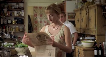 Movie still from “Funny Games” (1997), directed by Michael Haneke – A woman in a floral dress looking at an open newspaper; Medium shot, Over the shoulder angle